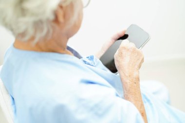 Evde bakım servisinde akıllı telefon kullanarak gözlük ya da görüş gözlüğü takan Asyalı son sınıf öğrencisi bir kadın..