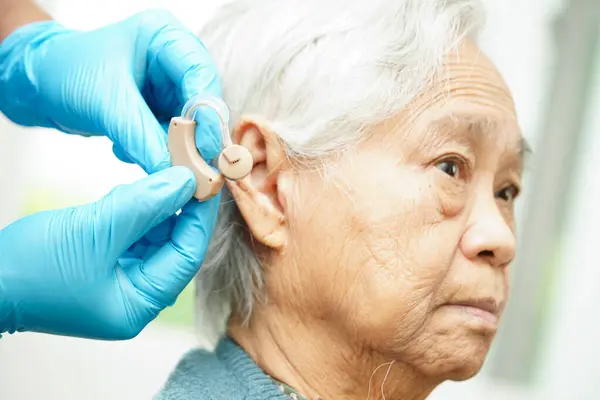 Doctor install hearing aid on senior patient ear to reduce hearing loss problem.