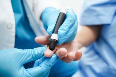 Asyalı doktor, kıdemli hasta parmağındaki tükenmez kalemle şeker seviyesini diyabet tedavisinde kontrol ediyor.