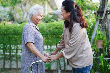 Bakıcı, Asyalı yaşlı kadın engelli hastaya parkta Walker 'la yürümesi için yardım ediyor..