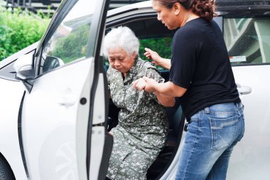 Bakıcı, Asyalı yaşlı kadın maluliyet hastasına arabasına binmesi için yardım ediyor..