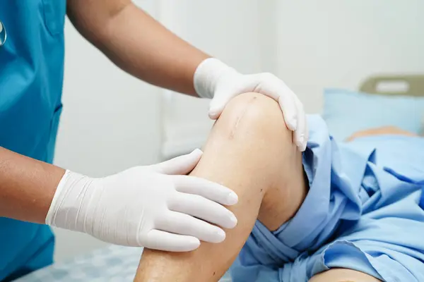 Doktor, hastanede dizinde yara izi olan Asyalı yaşlı kadın hastayı kontrol ediyor..