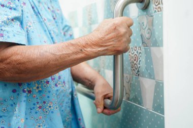 Asyalı yaşlı kadın hasta tuvalette tuvalet desteğini, tırabzan emniyet çubuğunu, hemşire hastanesinde güvenliği kullanıyor..