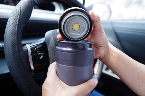 Asian woman driver hold thermo mug with hot coffee in car, dangerous and risk an accident.