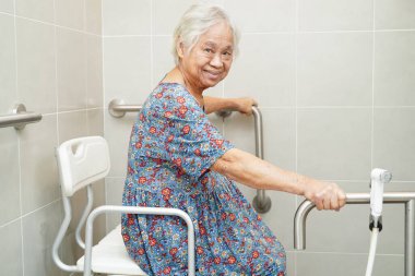 Asyalı yaşlı kadın hasta tuvalette tuvalet desteğini, tırabzan emniyet çubuğunu, hemşire hastanesinde güvenliği kullanıyor..