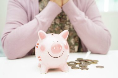 Emekli yaşlı kadın domuz kumbarasıyla bozuk para sayıyor ve aylık giderleri ve tedavi ücretini düşünüyor..