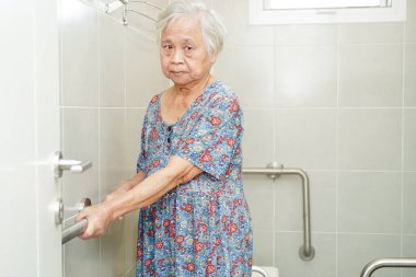 Asyalı yaşlı kadın hasta tuvalette tuvalet desteğini, tırabzan emniyet çubuğunu, hemşire hastanesinde güvenliği kullanıyor..