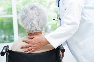 Bakıcı, hastanede tekerlekli sandalyede oturan Asyalı yaşlı kadın maluliyet hastasına yardım ediyor..