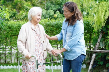 Bakıcı, parkta tekerlekli sandalyede oturan Asyalı yaşlı kadın maluliyet hastasına yardım ediyor..