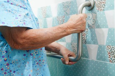 Asyalı yaşlı kadın hasta tuvalette tuvalet desteğini, tırabzan emniyet çubuğunu, hemşire hastanesinde güvenliği kullanıyor..