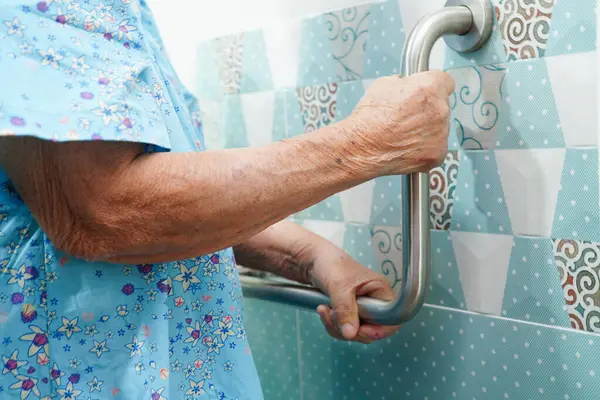 Asyalı yaşlı kadın hasta tuvalette tuvalet desteğini, tırabzan emniyet çubuğunu, hemşire hastanesinde güvenliği kullanıyor..