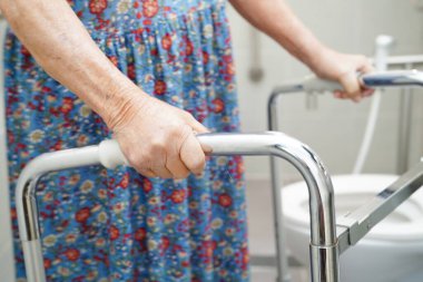 Asyalı yaşlı kadın hasta tuvalette tuvalet desteğini, tırabzan emniyet çubuğunu, hemşire hastanesinde güvenliği kullanıyor..