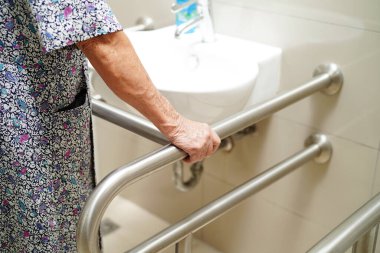 Asyalı yaşlı kadın hasta tuvalette tuvalet desteğini, tırabzan emniyet çubuğunu, hemşire hastanesinde güvenliği kullanıyor..