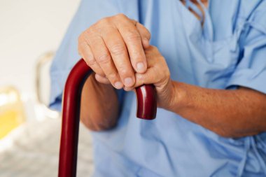 Hastanedeki Asyalı engelli kadın elinde kırışık bir değnekle yürüyen hasta..