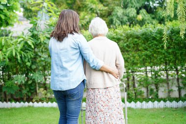 Bakıcı, Asyalı yaşlı kadın engelli hastaya parkta Walker 'la yürümesi için yardım ediyor..
