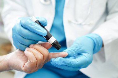 Asyalı doktor, kıdemli hasta parmağındaki tükenmez kalemle şeker seviyesini diyabet tedavisinde kontrol ediyor.