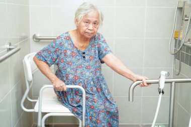 Asyalı yaşlı kadın hasta tuvalette tuvalet desteğini, tırabzan emniyet çubuğunu, hemşire hastanesinde güvenliği kullanıyor..