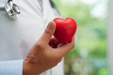 Asyalı kadın doktor hastanede sağlık için kırmızı kalp tutuyor..