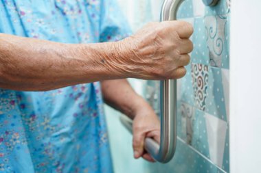 Asyalı yaşlı kadın hasta tuvalette tuvalet desteğini, tırabzan emniyet çubuğunu, hemşire hastanesinde güvenliği kullanıyor..