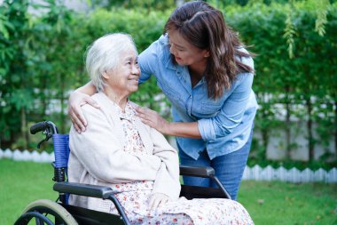 Bakıcı, hastanede tekerlekli sandalyede oturan Asyalı yaşlı kadın maluliyet hastasına yardım ediyor..