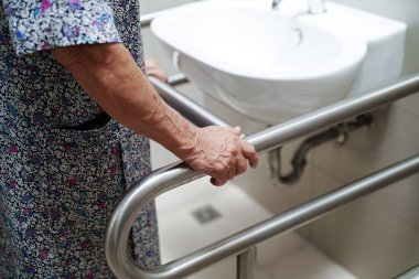 Asyalı yaşlı kadın hasta tuvalette tuvalet desteğini, tırabzan emniyet çubuğunu, hemşire hastanesinde güvenliği kullanıyor..