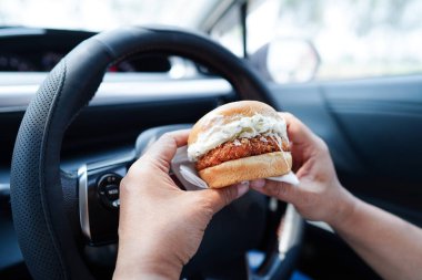Asyalı kadın sürücü arabada hamburger yiyip, tutar, tehlikeli ve kaza riskini göze alır..