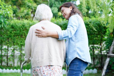 Doktor, Asyalı yaşlı kadın engelli hastaya parkta yürüme konusunda yardım ediyor..