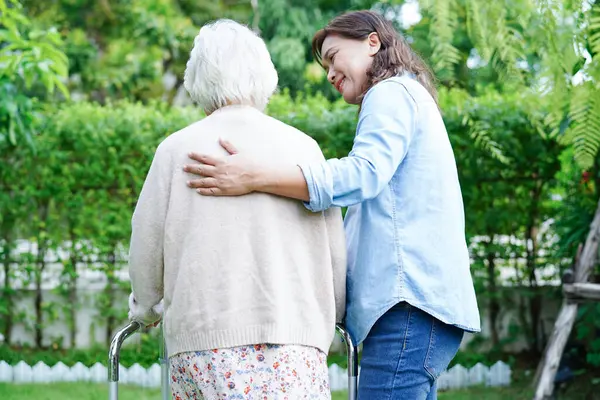 Doktor, Asyalı yaşlı kadın engelli hastaya parkta yürüme konusunda yardım ediyor..