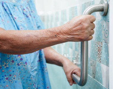 Asyalı yaşlı kadın hasta tuvalette tuvalet desteğini, tırabzan emniyet çubuğunu, hemşire hastanesinde güvenliği kullanıyor..