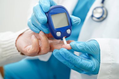 Diyabet tedavisinde kan şekeri seviyesini kontrol etmek için dijital glikoz ölçer kullanan Asyalı doktor.