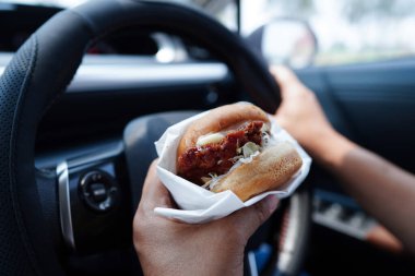Asyalı kadın sürücü arabada hamburger yiyip, tutar, tehlikeli ve kaza riskini göze alır..