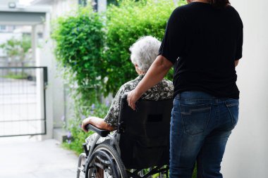 Bakıcı, hastanede tekerlekli sandalyede oturan Asyalı yaşlı kadın maluliyet hastasına yardım ediyor..