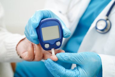 Diyabet tedavisinde kan şekeri seviyesini kontrol etmek için dijital glikoz ölçer kullanan Asyalı doktor.