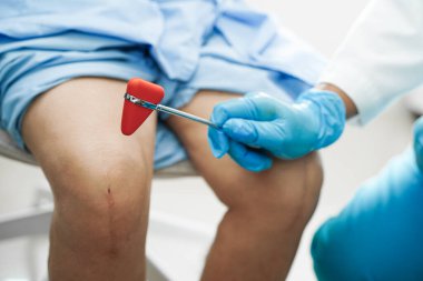 Asyalı doktor, hastanedeki yaşlı hastayı muayene etmek için diz refleksi sinirine vurdu..