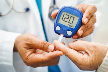 Diyabet tedavisinde kan şekeri seviyesini kontrol etmek için dijital glikoz ölçer kullanan Asyalı doktor.