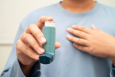 Astım ve kronik obstrüktif akciğer hastalığı COPD, Asyalı genç adam ölçülü doz solunum cihazı kullanıyor..