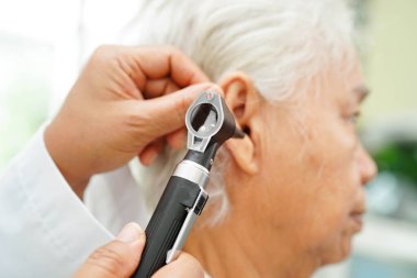 Otolaryngologist ya da ENT hekim doktoru yaşlı hasta kulağını otoskopla muayene ediyor, işitme sorunu var..