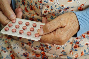 Asyalı yaşlı bir kadın elinde hap tutuyor, güçlü ve sağlıklı bir ilaç..