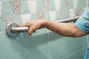 Asyalı yaşlı kadın hasta tuvalette tuvalet desteğini, tırabzan emniyet çubuğunu, hemşire hastanesinde güvenliği kullanıyor..