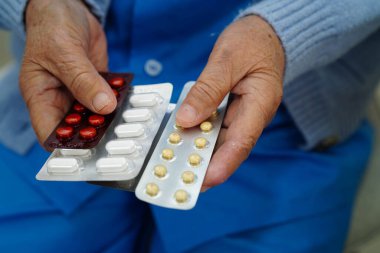 Asyalı yaşlı bir kadın elinde hap tutuyor, güçlü ve sağlıklı bir ilaç..