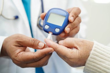 Diyabet tedavisinde kan şekeri seviyesini kontrol etmek için dijital glikoz ölçer kullanan Asyalı doktor.