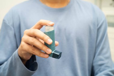 Astım ve kronik obstrüktif akciğer hastalığı COPD, Asyalı genç adam ölçülü doz solunum cihazı kullanıyor..