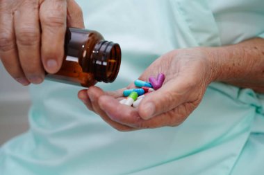 Asyalı yaşlı kadın elinde hap kapsülü ilacı tutuyor..