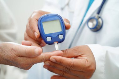 Diyabet tedavisinde kan şekeri seviyesini kontrol etmek için dijital glikoz ölçer kullanan Asyalı doktor.