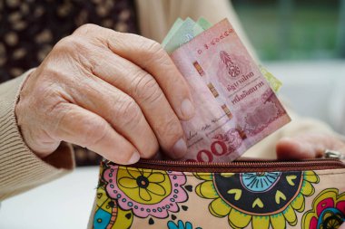 Asyalı yaşlı ya da yaşlı kadın para sayıyor. Yoksulluk, emeklilikte tasarruf sorunu.