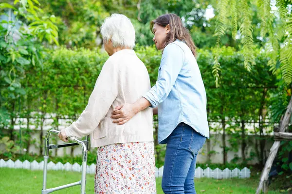Bakıcı, Asyalı yaşlı kadın engelli hastaya parkta Walker 'la yürümesi için yardım ediyor..