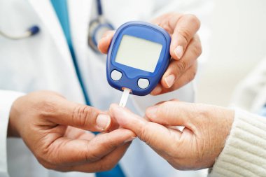 Diyabet tedavisinde kan şekeri seviyesini kontrol etmek için dijital glikoz ölçer kullanan Asyalı doktor.