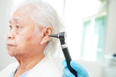 Otolaryngologist ya da ENT hekim doktoru yaşlı hasta kulağını otoskopla muayene ediyor, işitme sorunu var..