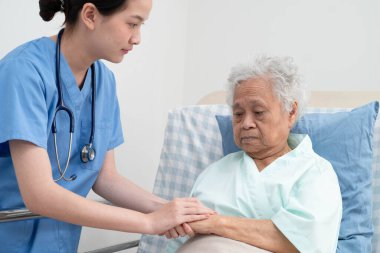 Asyalı doktor yaşlı kadın hasta sağlığını hastanede kontrol edip tedavi ediyor.