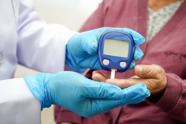 Diyabet tedavisinde kan şekeri seviyesini kontrol etmek için dijital glikoz ölçer kullanan Asyalı doktor.